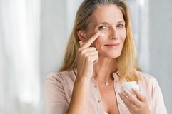 Frau vor dem Spiegel cremt sich Gesicht ein
